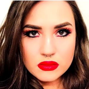 A person with long dark hair and a nose ring wearing makeup