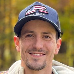 A person with a goatee smiling outside wearing a blue cap