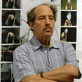 a man with a mustache wearing a short sleeved and arms folded stands in front a photo prints