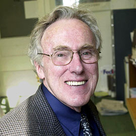 headshot of a man with glasses wearing a blue shirt and plaid jacket