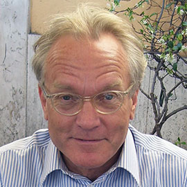 headshot of a man with blond hair and glasses wearing a blue striped shirt