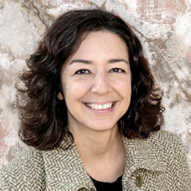 a woman with curly dark hair wearing a houndstooth jacket