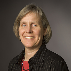 headshot of a woman with brown hair wearing a dark shirt and necklace
