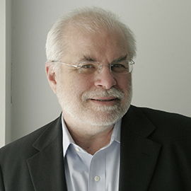 headshot of a man with white hair and beard in glasses and wearing a dark suit coat and white shirt