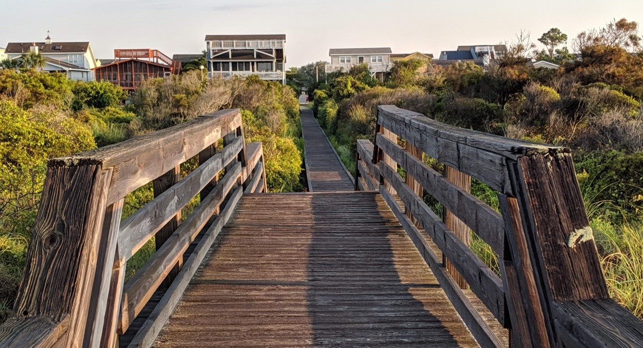 A wooden bridge leading to a row of houses surrounded by trees.