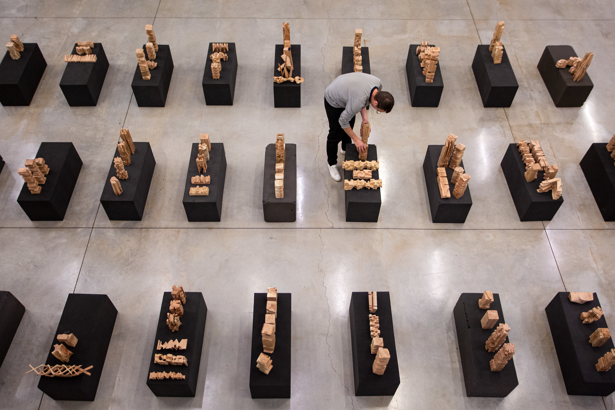 A person setting up architectural models on black pedestals.