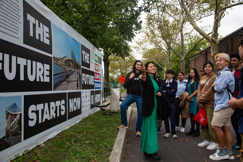 a group of people observing a person speaking and showcasing a mural behind them