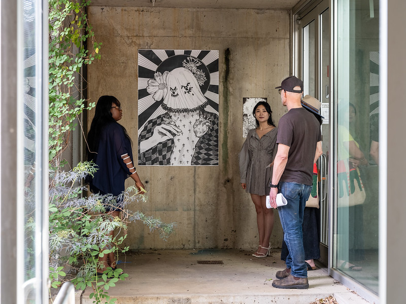 a group of people standing together observing an artwork hung on the wall