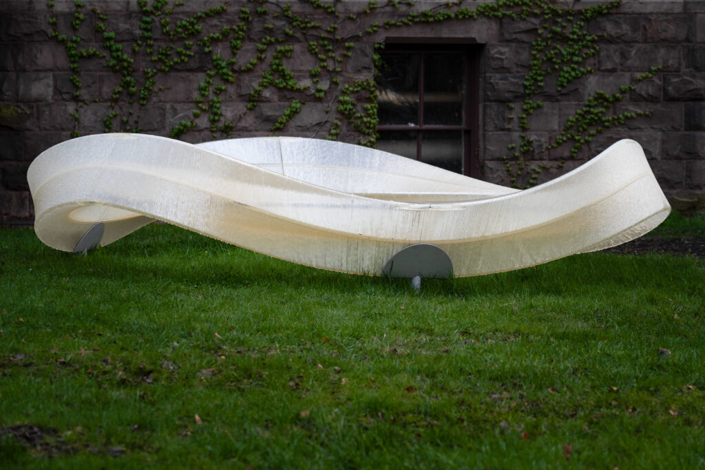 a 3d printed closed loop structure resting upon pedestals stuck in the grass
