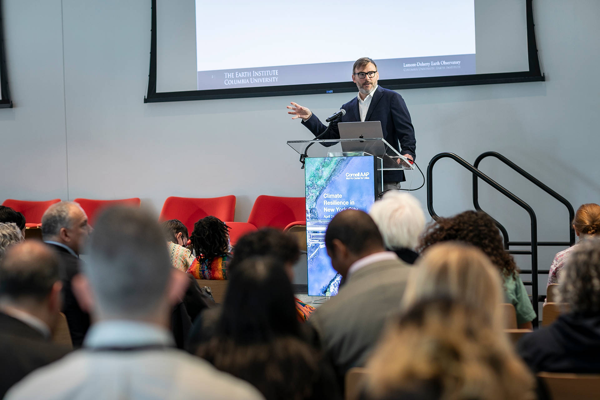 Man lecturing behind a podium to gathered crowd