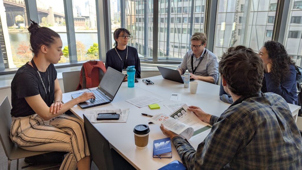 Several people sitting at a table with laptops, books, and working materials.