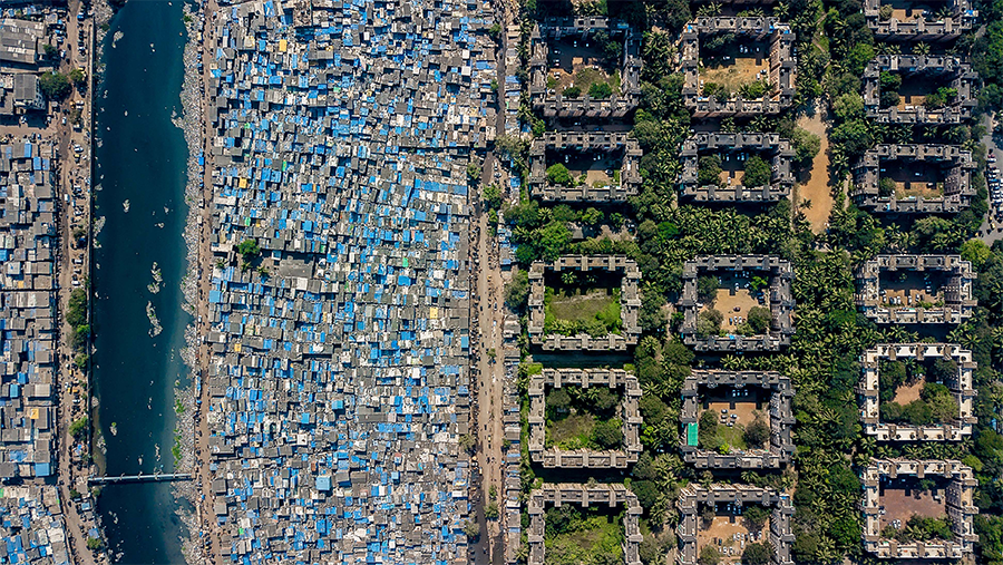 rows of sheet metal housing with blue roofs and large luxury concrete buildings next to them