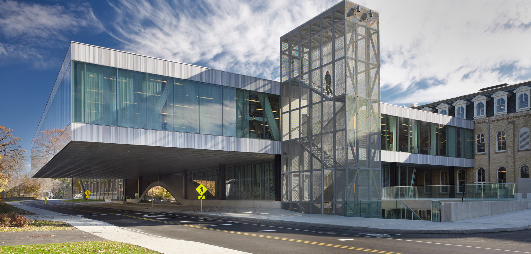 A modern glass building cantilevered over a road with a metal stair tower attached