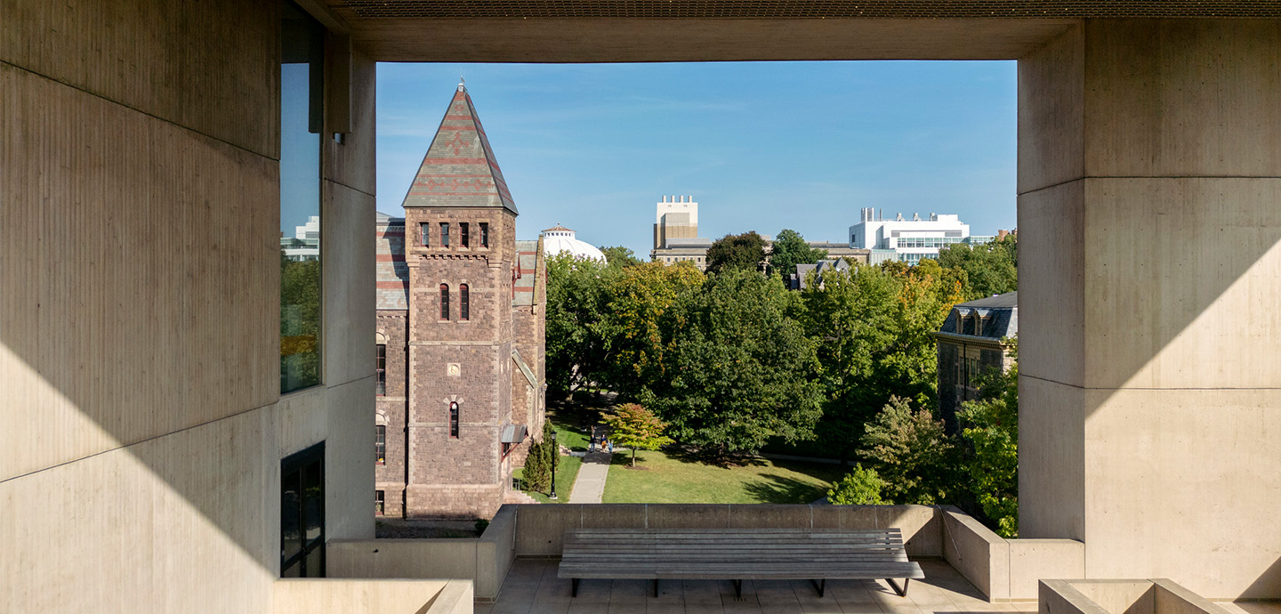 Large building framing a brick clock tower on a sunny day on a college campus
