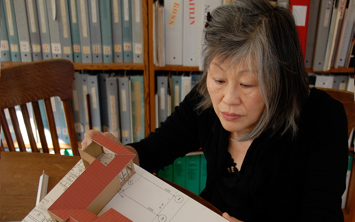 A person with a black shirt sitting in front of a bookshelf observing a model.