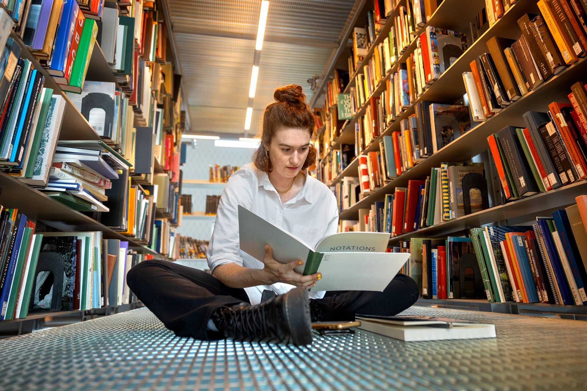 student seated on the floor between book stacks