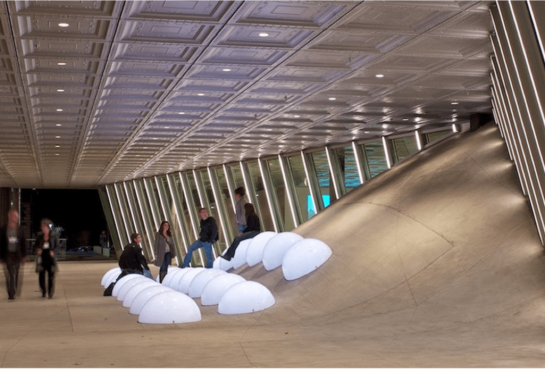 people in a concrete corridor seated on lit plastic domes
