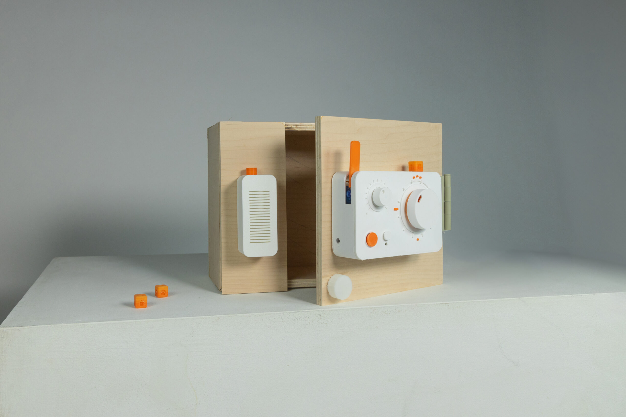 A rectangular device with buttons, rotationg knobs, and small cubic attachable pieces placed on a small cabinet door.