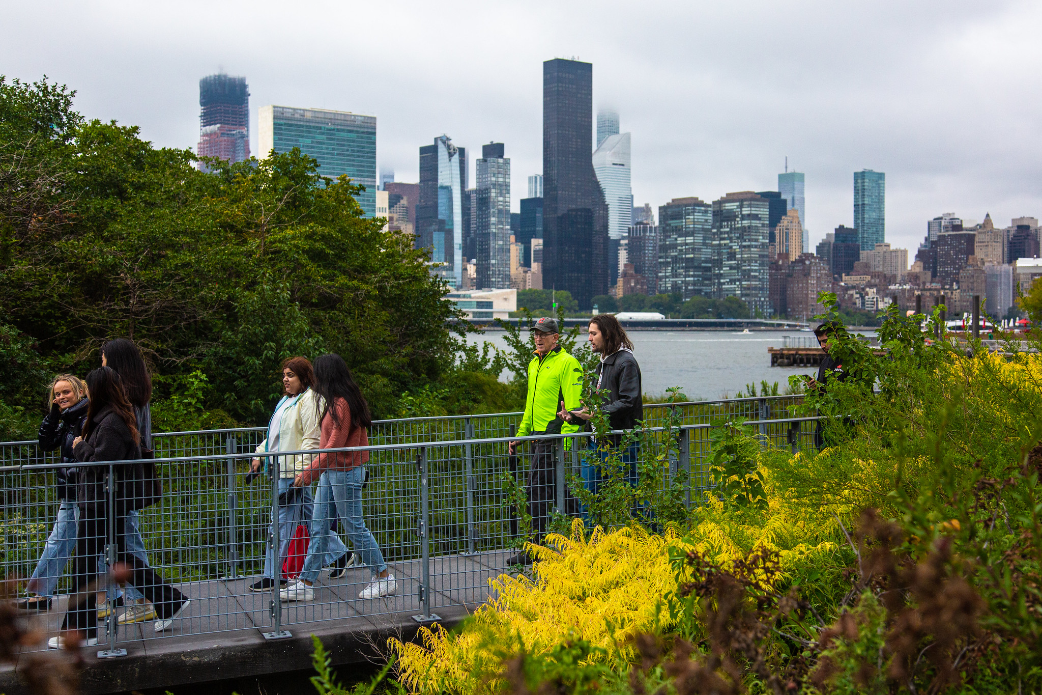 People walking across a footbridge with the New York City skyline at rear