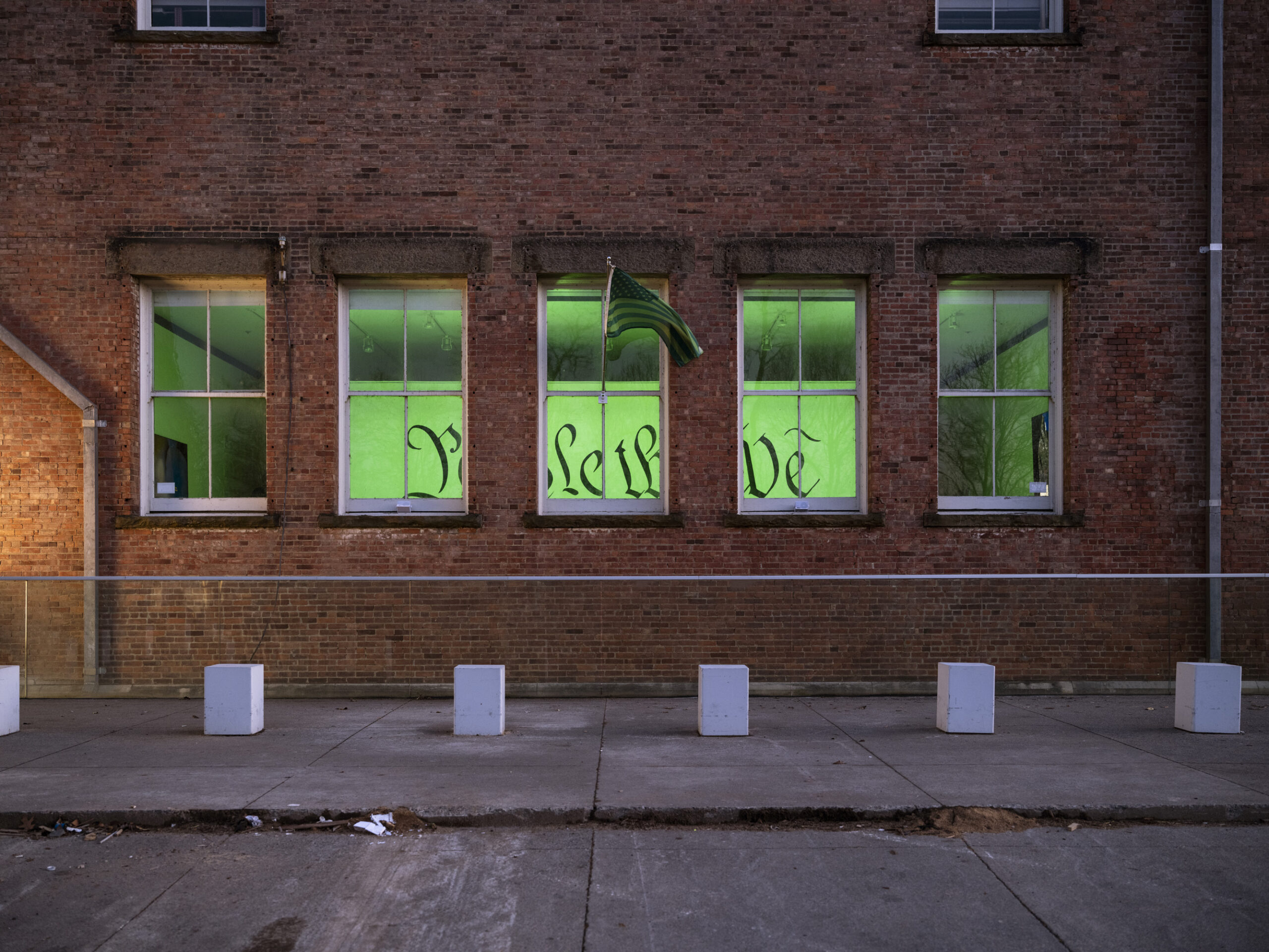 An outside view of a brick building with five windows showing a glimpse of the words 
