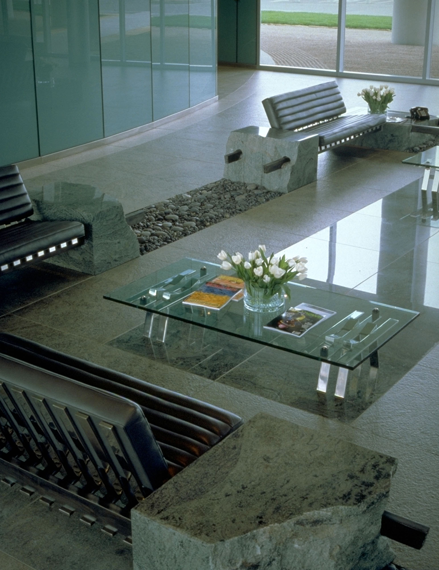 Interior view of a lobby designed with matte stone surfaces accented by a glass table on an inlay of shiny tile.