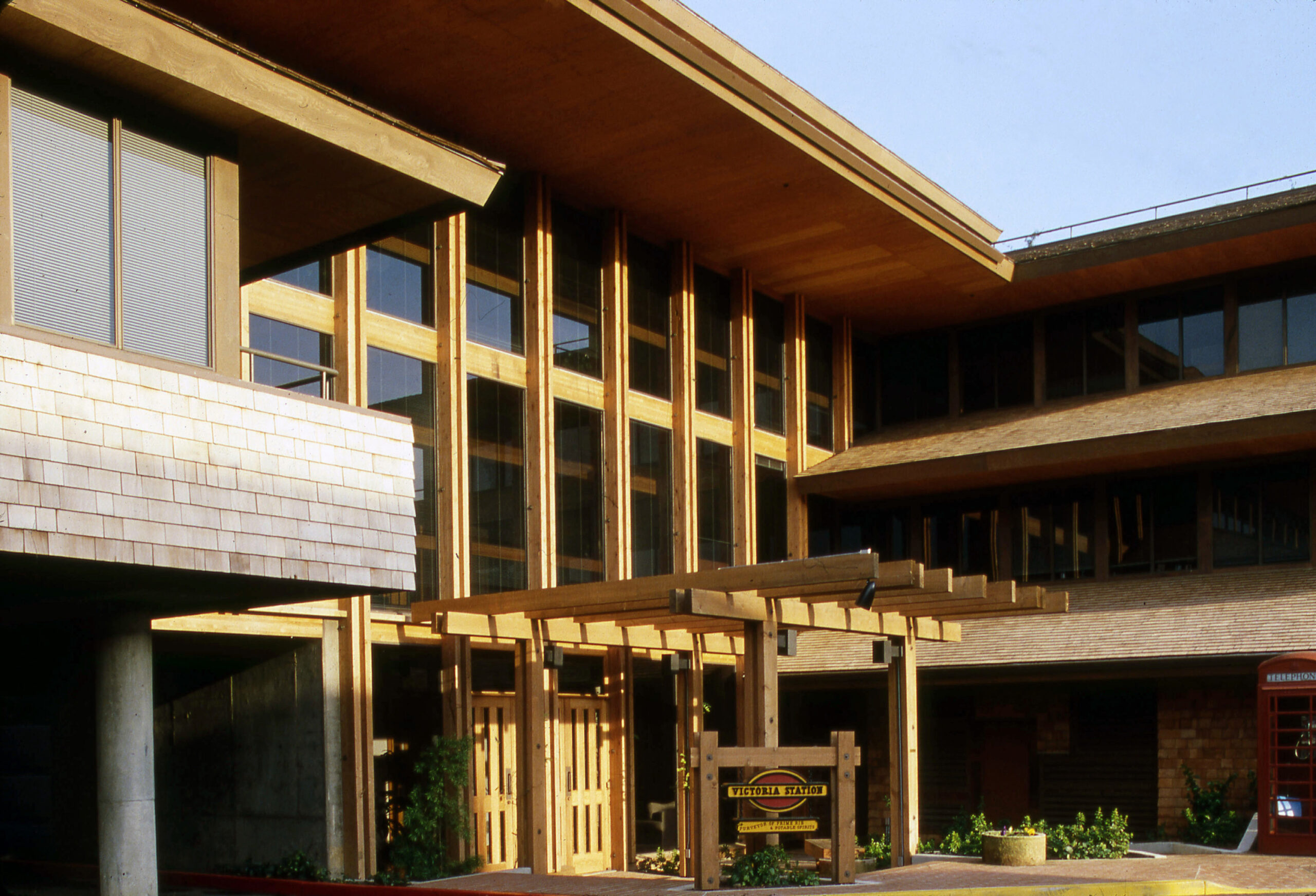 A pergola frames the entrnace to a multistory building lined with windows bordered by wooden planks.
