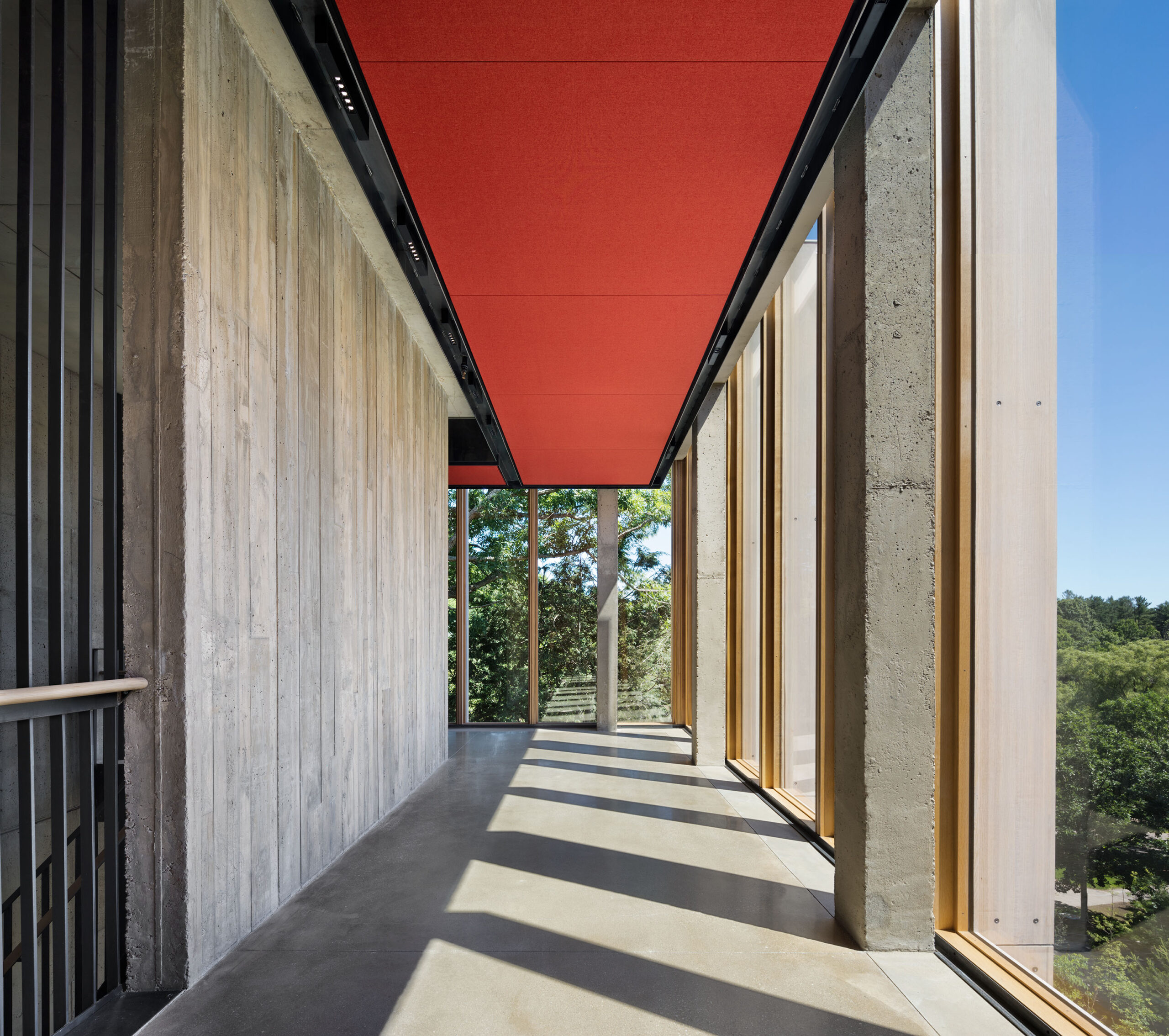 A neutral-colored hallway features a red ceiling, a wall lined vertically with wooden planks, and an exterior wall lined with windows.