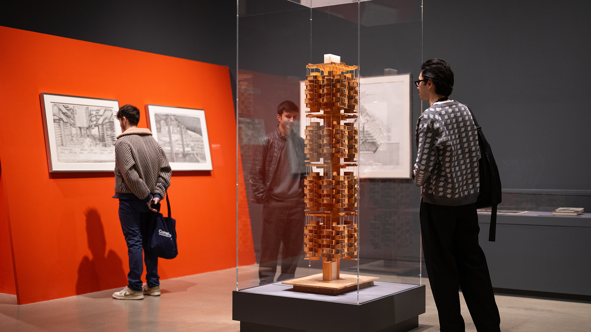 People explore an architectural model encased in glass at a museum.