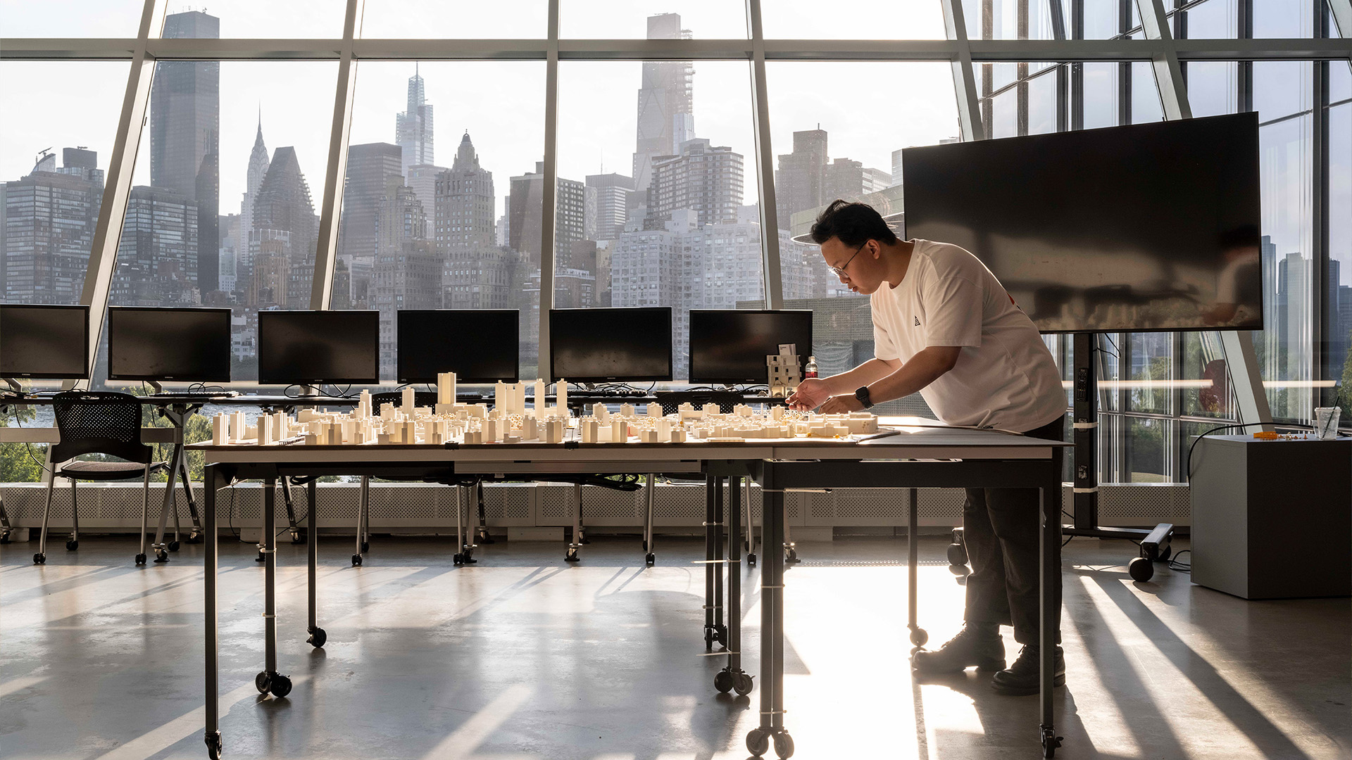 A person adjusts a model that is sitting on a table inside a glass walled classroom.