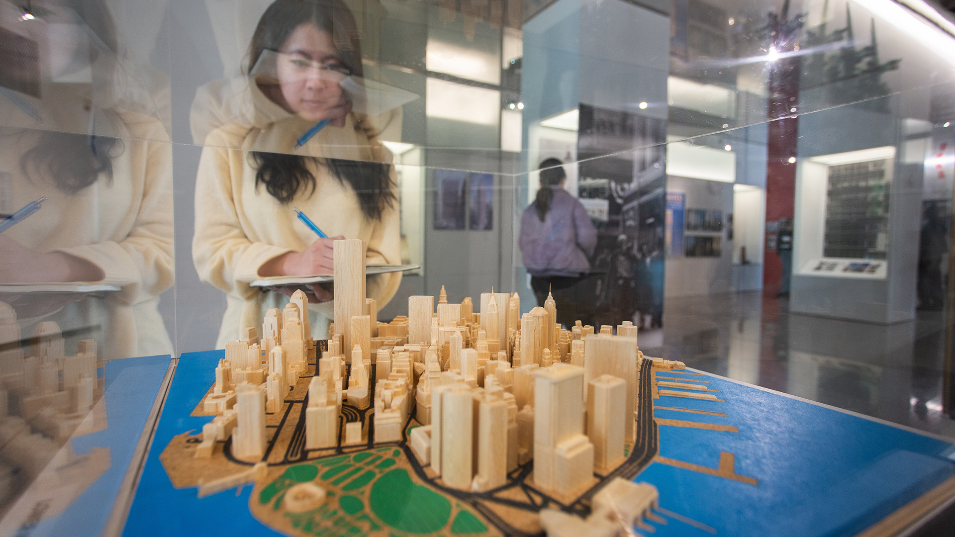 A person looks inside an architectural model encased in glass at a museum.
