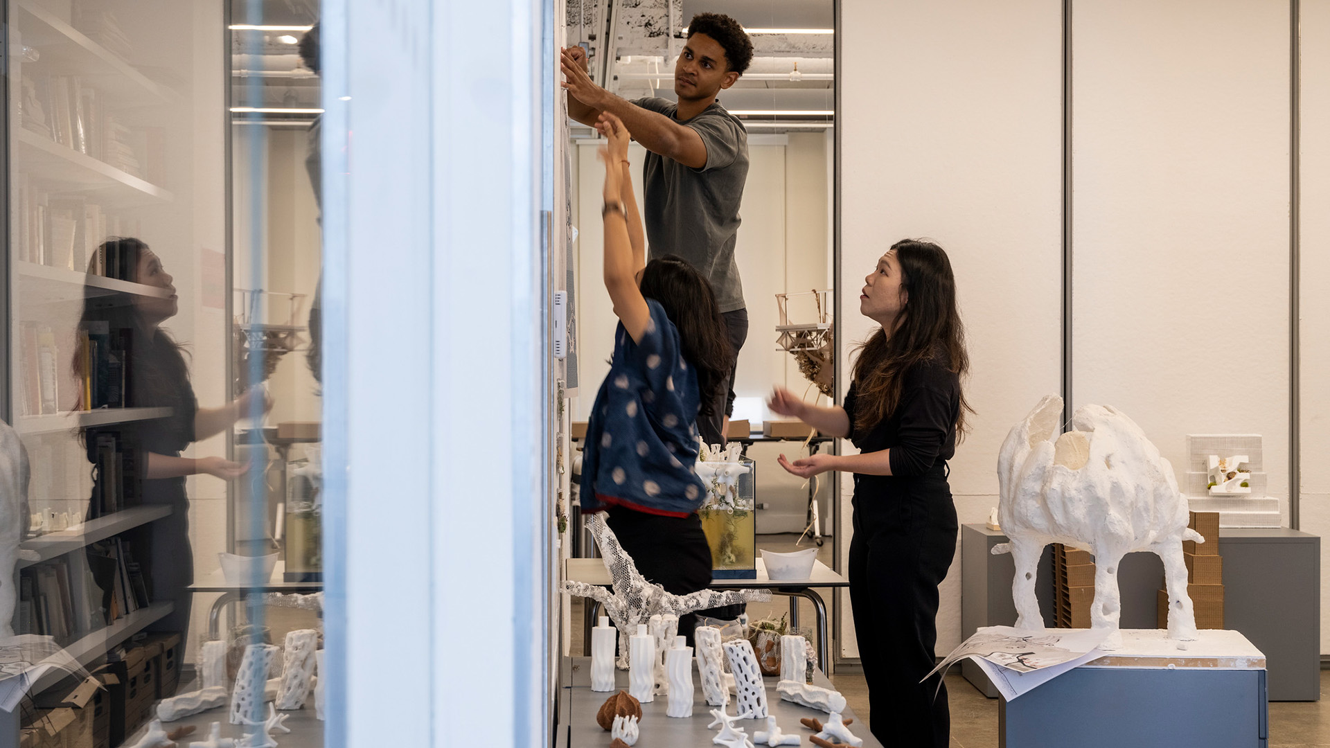 Three people attach their architectural drawings to a wall.