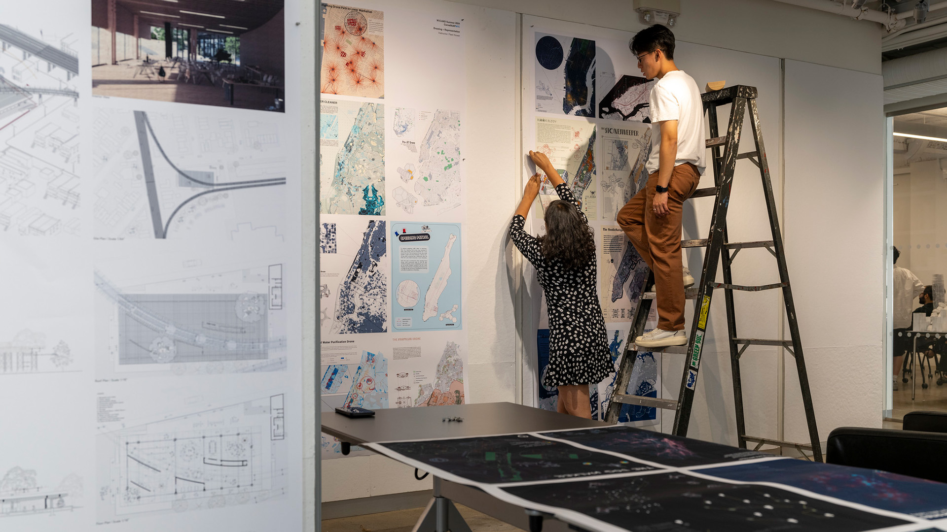 Two people attach renderings of maps to the wall.