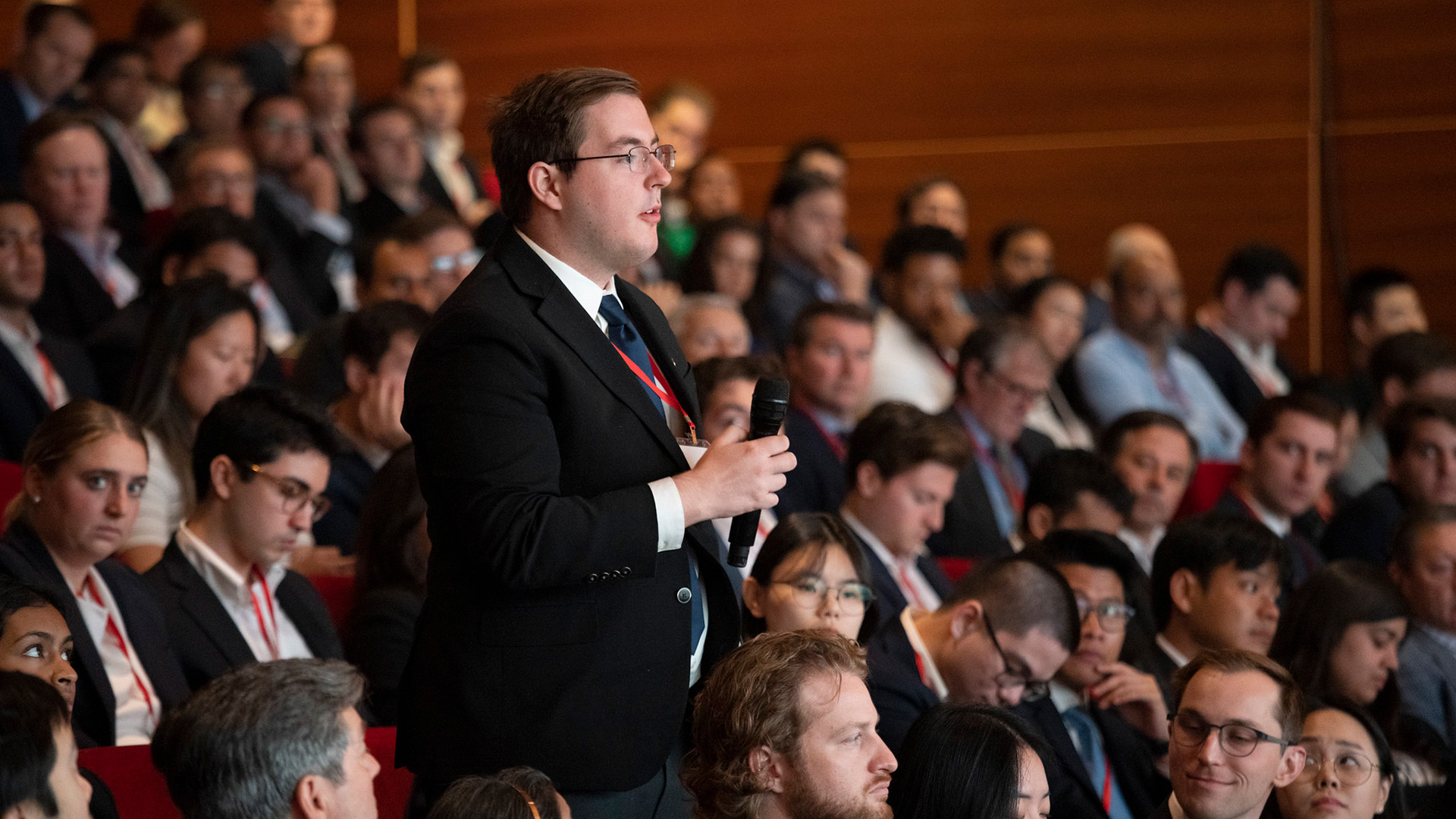 A person stands in an audience to ask a question with a microphone.