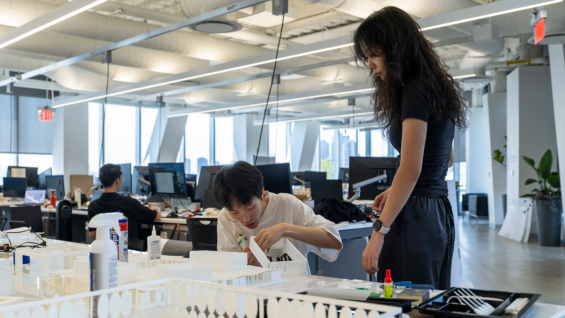 A person adjusts an architectural model while another person watches them.