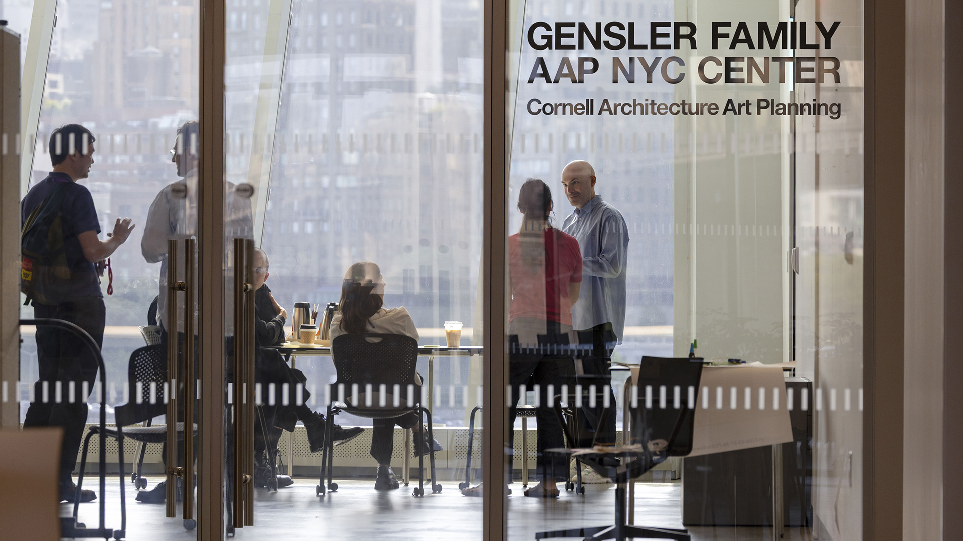 A view inside a glass-walled classroom with people casually talking to each other.