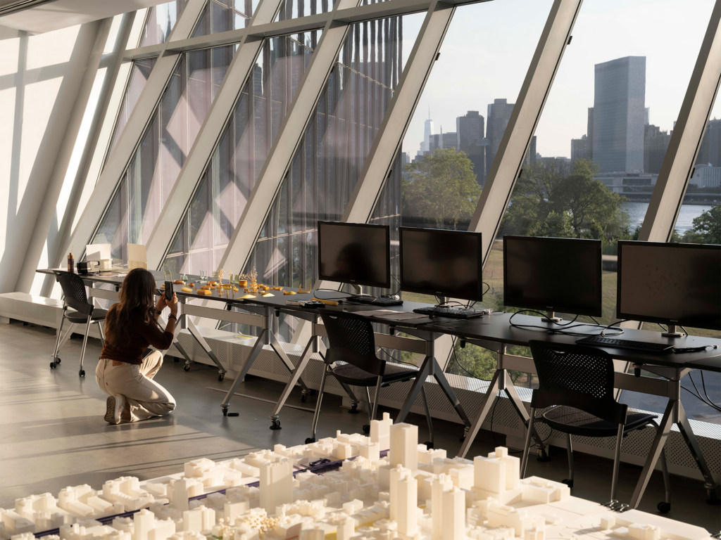 Student taking a photo of a model with the NYC skyline visible through large windows