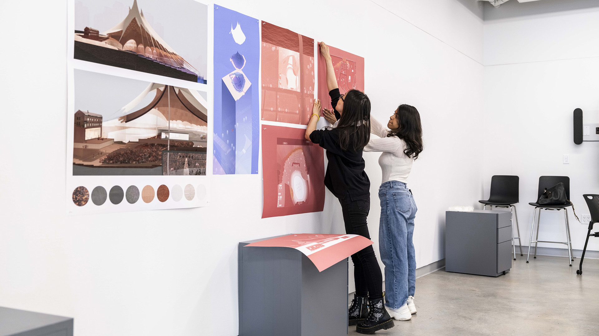 Two people attach their architectural drawings to the wall.