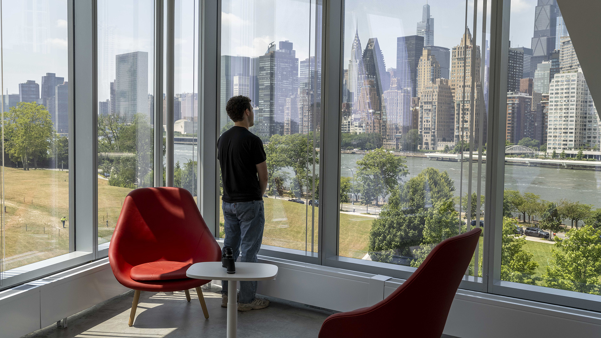 A person looks out of a glass-walled room toward the New York City skyline.