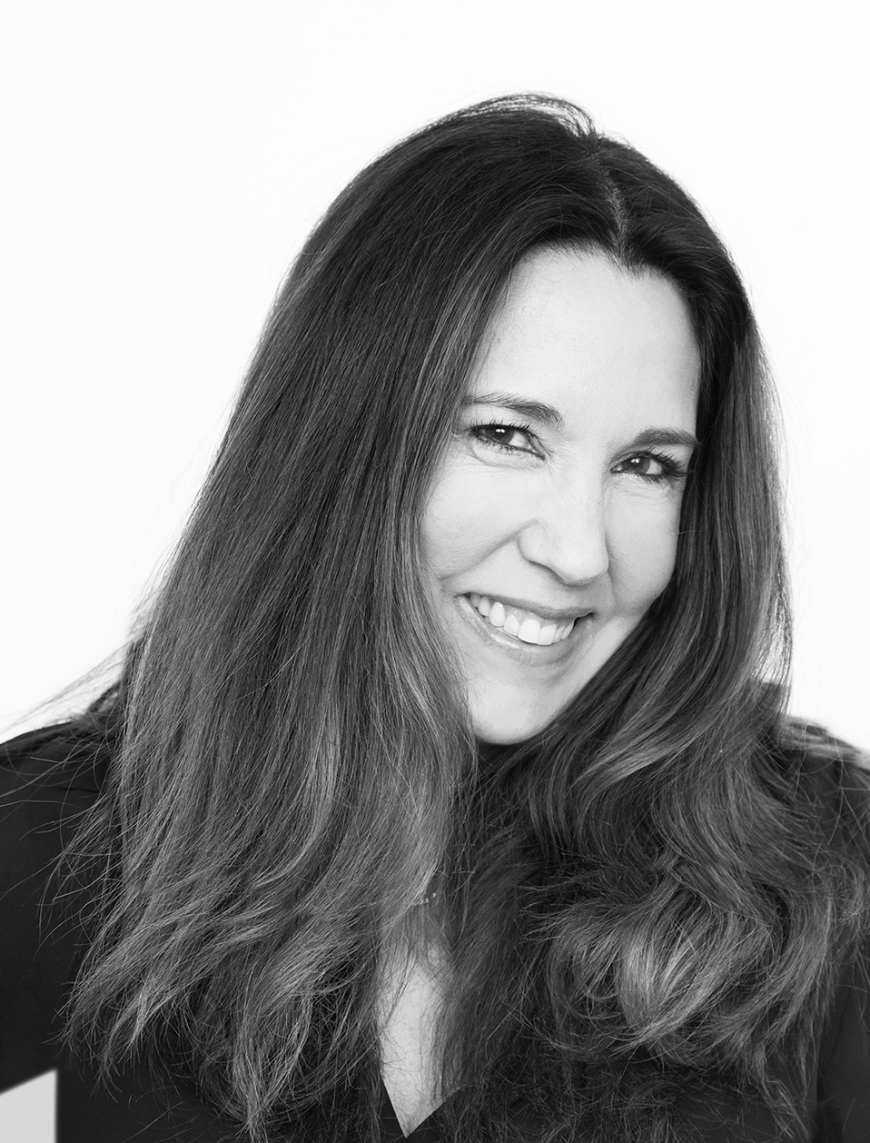 Professional, black-and-white image of a woman with long hair, wearing a black long-sleeved shirt.
