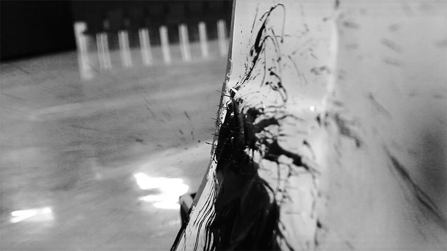 Close up of an ink splatter with needles poking through the saturated piece of paper.