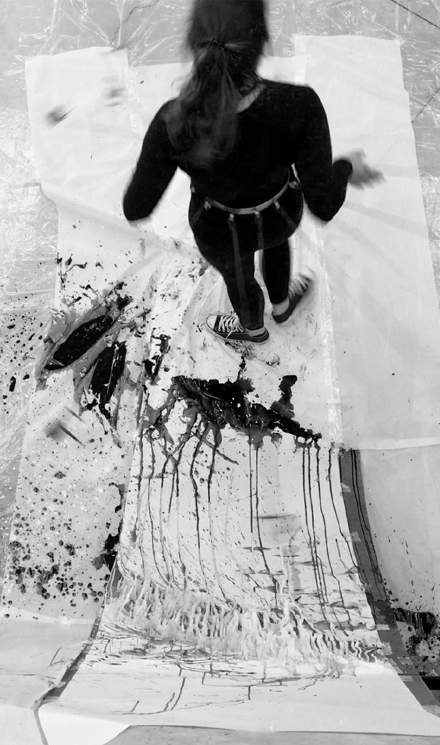 Ink-filled balloons are attached to long sticks that are fastened around a person's belt. The balloons are popping against a needle-filled piece of paper.