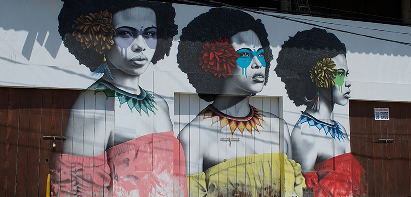 A mural of three women with afro hairstyles, adorned with colorful flowers and face paint, symbolizing themes of racial injustice.