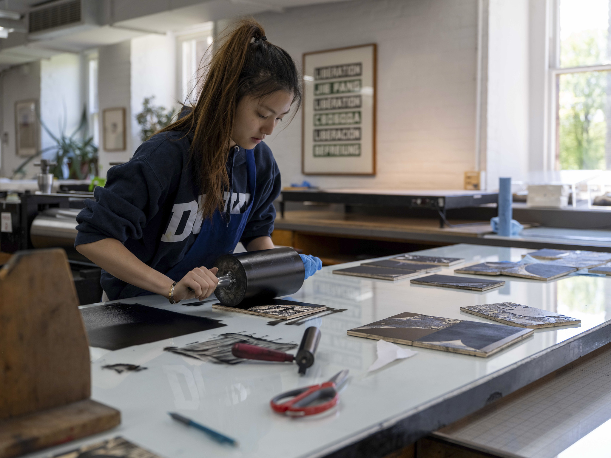 A person uses a brayer to roll ink over a linoleum stamp.