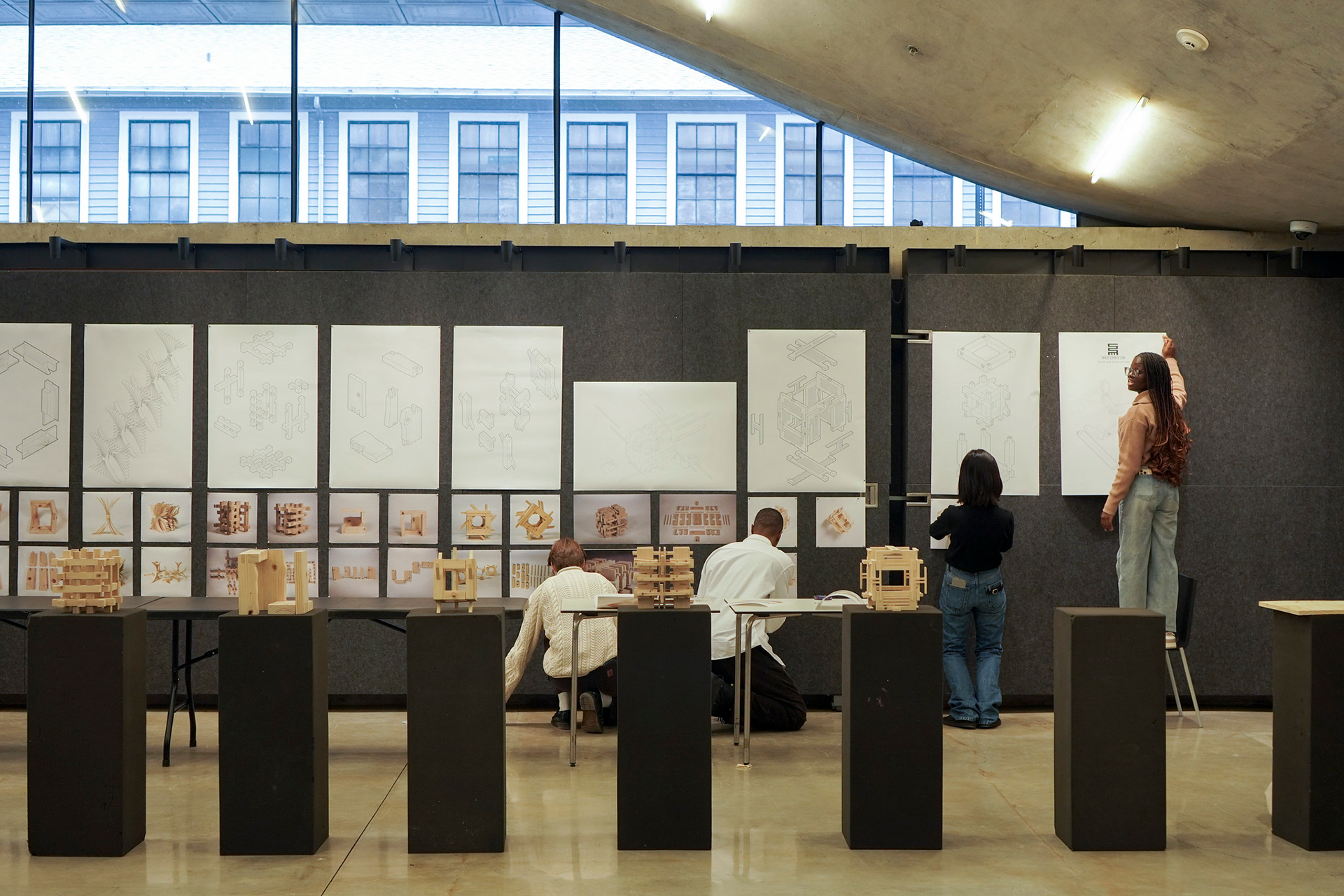 Four people pin their posters to a wall.