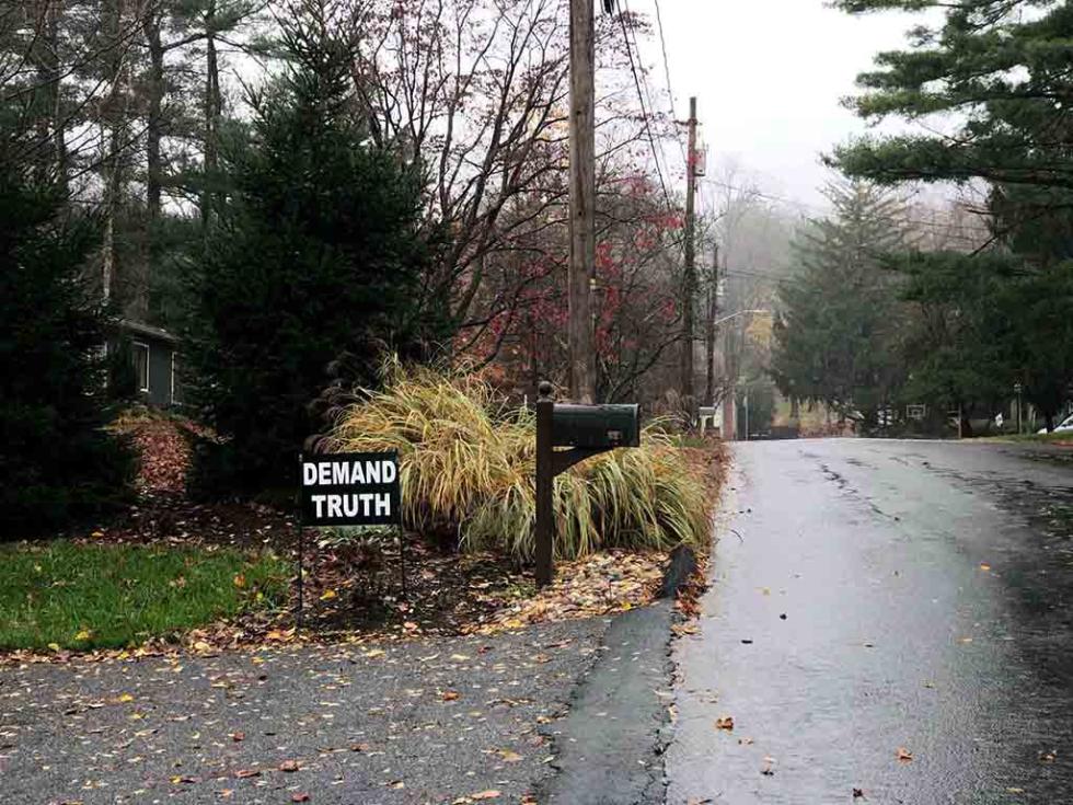 A residential street and mailbox with a yard sign that reads 