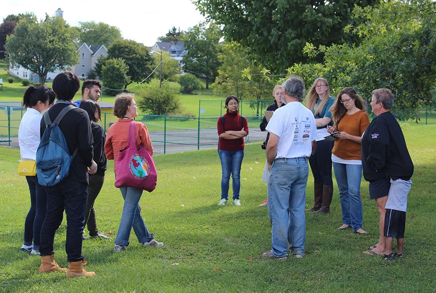 A group of people stand in a circle while outside on the grass.