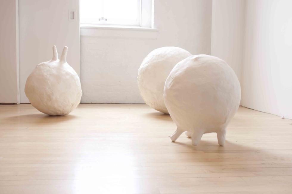 Three white bulbous sculptures sit on the wood floor.