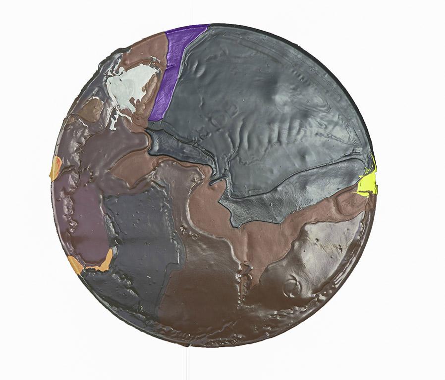 A circle of poured acrylic paint that is black, brown, and purple with a speck of yellow.