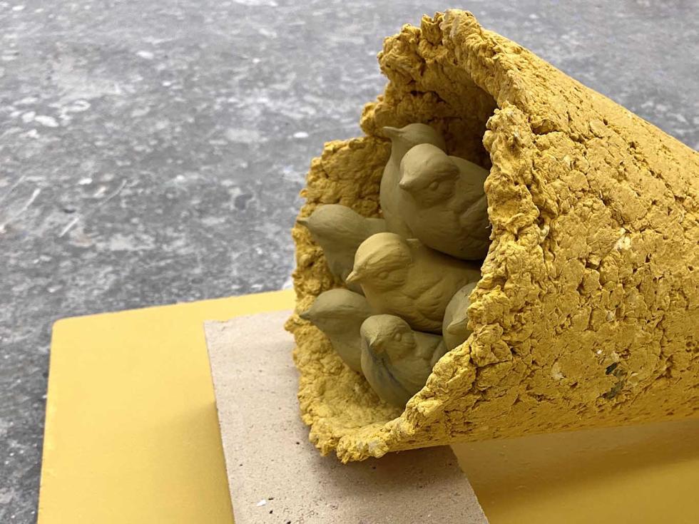 A yellow platform with a yellow cone on its side, with molds of birds inside the cone.