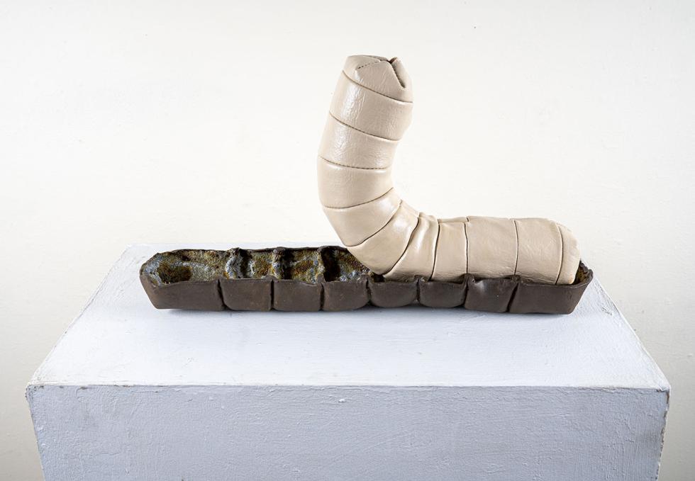 Caterpillar-like sculpture emerges from chrysalis-like base.